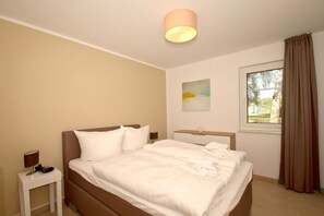A bedroom with a bed, bedside table, lamp, and a window with curtains.