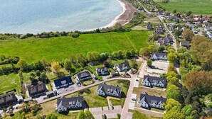 Oversigtsbillede af et kystnære boligområde med huse, en strand og grønne marker.