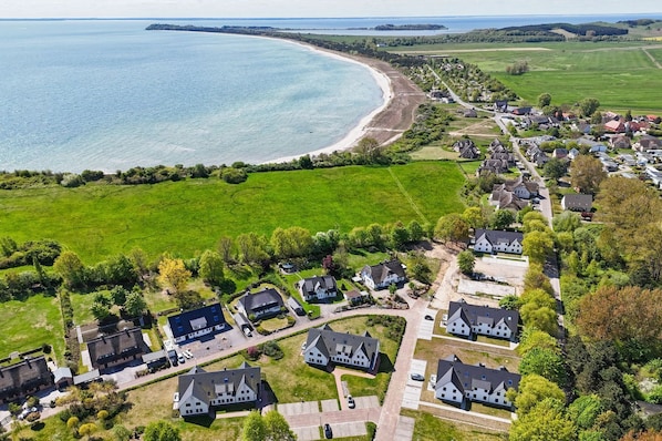 An aerial view of a coastal residential area with houses, green fields, and a beach.