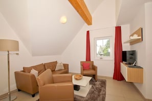 Een moderne woonkamer met een bruine leren bank, een witte salontafel, een rode fauteuil en een tv op een houten dressoir.