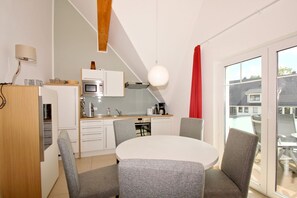 Eine moderne Küche mit weißen Schränken, einer Mikrowelle und einem Essbereich mit rundem Tisch und grauen Stühlen.