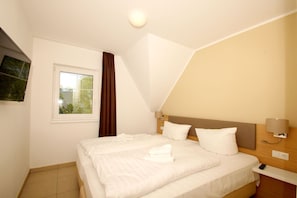 Una habitación de hotel con cama, ventana, televisor de pared y mesita de noche con lámpara.