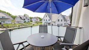 A balcony with a table and chairs, a blue umbrella, and a view of houses in the background. - Beachfront vacation rental with a balcony, access to the pool and sauna - Rex Rugia - Rex Rugia (Göhren)