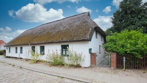 Une maison de campagne traditionnelle, avec ses murs blanchis à la chaux, son toit de chaume, son portail en briques et sa rue pavée.
