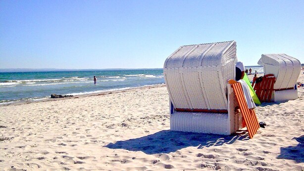 Des chaises de plage en matière tissée, sur une plage de sable, avec l’océan en arrière-plan.