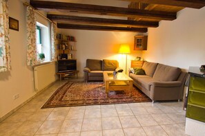 A cozy living room with a sofa, a coffee table, a TV, and a lamp. - Waterfront house with a deck and garden - Ferienhaus Storchennest Haus R - (Wiek)
