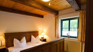 Une chambre à coucher avec un lit en bois, une table de chevet avec une lampe, une fenêtre avec des rideaux et un radiateur.