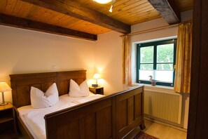 A bedroom with a wooden bed, a nightstand with a lamp, a window with curtains, and a radiator. - Waterfront house with terrace and garden - Ferienhaus Storchennest Haus R - (Wiek)