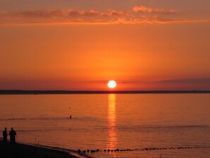 A sunset over a calm body of water with a few people standing on the shore. - Waterfront house with terrace and garden - Ferienhaus Storchennest Haus R - (Wiek)