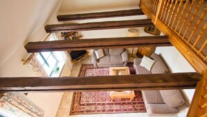 Un escalier dont les poutres en bois sont apparentes mène à un salon comprenant un canapé, une table basse et un tapis à motifs.
