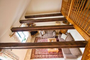 Una escalera con vigas de madera a la vista que lleva a una sala de estar con un sofá, una mesa de centro y un tapete estampado.