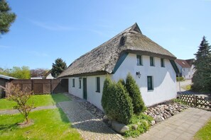 A traditional house with a thatched roof, white walls, and a small garden with a pathway leading to the entrance. - Waterfront house with terrace and garden - Ferienhaus Storchennest Haus R - (Wiek)