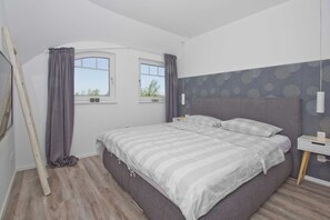 A bedroom with a bed, two windows, a headboard, and a bedside table. - At the sailing marina, with a patio, garden, and ocean view—Boddentraum Abendrot vacation home— (Gager)
