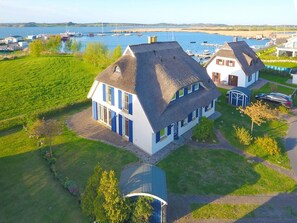 A large house with a thatched roof, surrounded by a well-maintained lawn and a view of the sea. - At the sailing harbor, terrace, garden, sea view - vacation home Boddentraum Abendrot - (Gager)