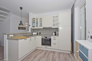 A modern kitchen with white cabinetry, a built-in oven, and a wooden countertop. - At the sailing marina, with a patio, garden, and ocean view—Boddentraum Abendrot vacation home— (Gager)