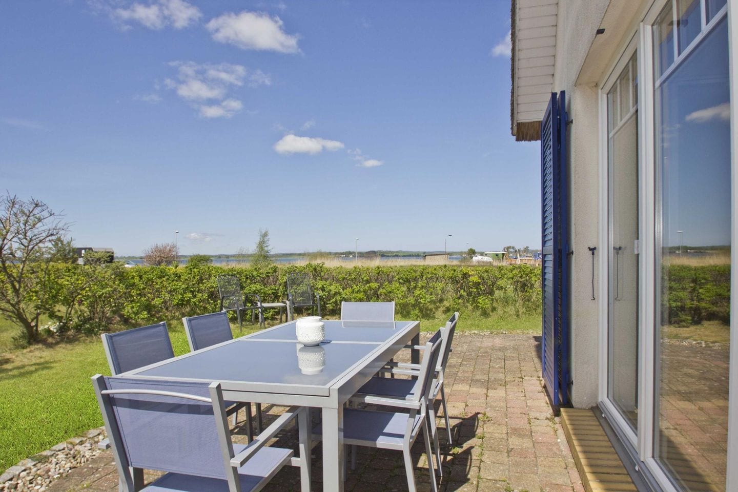Eine Terrasse im Freien mit Tisch und Stühlen, einer Glastür und Blick auf die Landschaft.
