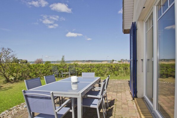 An outdoor patio with a table and chairs, a glass door, and a view of the landscape.