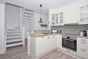 A modern kitchen with white cabinets, a Bosch oven, a sink, and a wooden countertop. - At the sailing harbor, terrace, garden, sea view - vacation home Boddentraum Abendrot - (Gager)