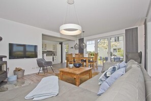A modern living room with a large sofa, a wooden coffee table, and a TV mounted on the wall. - At the sailing marina, with a patio, garden, and ocean view—Boddentraum Abendrot vacation home— (Gager)