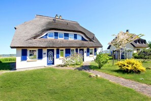 A traditional house with a thatched roof, blue shutters, and a well-maintained garden. - Near the marina, with a patio, garden, and ocean view—Boddentraum Morgenrot vacation home— (Gager)