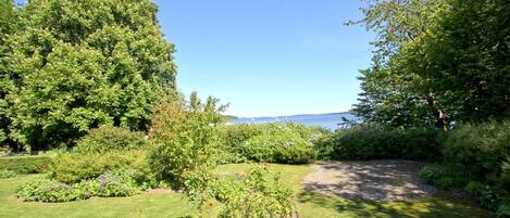 A well-maintained garden with a variety of plants and flowers, a clear sky, and a view of the sea in the background.