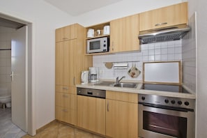 A compact kitchen with wooden cabinets, a microwave, a kettle, a coffee maker, a sink, and an oven. - 2-room vacation apartment with a view of the sea from the balcony - Villa Vilmblick FeWo 15 - Villa (Putbus)