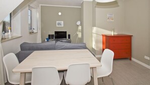 Un salon moderne avec un canapé, une table à manger et des chaises, un téléviseur et une commode rouge.