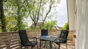 Une terrasse extérieure avec une table et quatre chaises, entourée de rampes en bois et d’arbres.