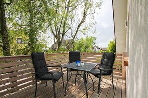 Una terraza al aire libre con una mesa y cuatro sillas, rodeada de barandas de madera y árboles.
