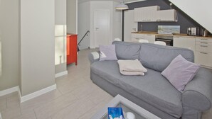 Un salon moderne avec un canapé gris, une table basse et une cuisine en arrière-plan.