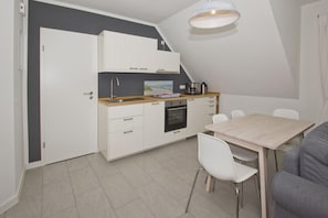 A compact kitchenette with white cabinets, a sink, and a small oven. There is a dining table with chairs and a light fixture above. - Liesi Vacation Apartment—quiet location, beautiful scenery, close to the Baltic Sea— (Putbus)