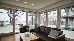A spacious living room with a large window, a brown leather sofa, a wooden coffee table, and a chair.