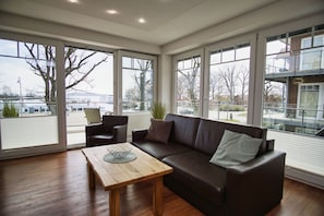 Ein geräumiges Wohnzimmer mit großem Fenster, einem braunen Ledersofa, einem Holztisch und einem Sessel.