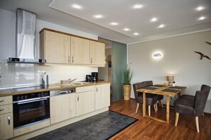 A modern kitchen with wooden cabinets, a built-in oven, and a dining area with a wooden table and chairs. - Hafenresidenz Lauterbach Wohnung 2-3 - Hafenresidenz (Putbus)