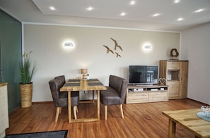 A modern living room with a wooden dining table, two leather sofas, a TV, and a wooden cabinet. - Hafenresidenz Lauterbach Wohnung 2-3 - Hafenresidenz (Putbus)