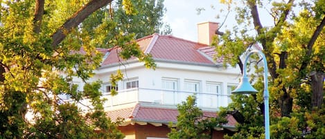 A two-story building with a red-tiled roof, surrounded by lush green trees.