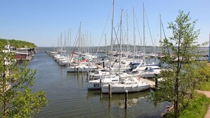 A marina with numerous boats docked along a narrow waterway, surrounded by greenery and a clear sky.