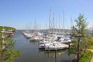 Ein Yachthafen mit zahlreichen Booten, die an einem schmalen Kanal liegen, umgeben von Grünflächen und blauem Himmel.