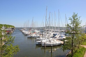 A marina with numerous boats docked along a narrow waterway, surrounded by greenery and a clear sky.