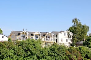 A row of multi-story houses with balconies, surrounded by dense greenery. - Right behind the dune, with a balcony and a view of the sea - Strandvilla B öck FeWo 10 - (Glowe)