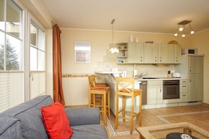 A compact living space with a kitchenette, a dining area, and a sofa with a red pillow. - Right behind the dune, with a balcony and a view of the sea - Strandvilla Böck FeWo 10 - (Glowe)