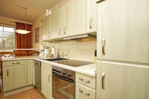 A kitchen with light-colored cabinets, a stove, a sink, and a coffee maker.