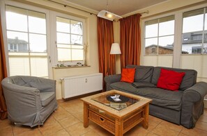 A living room with a grey sofa, a wooden coffee table, and a window with curtains. - Right behind the dune, with a balcony and a view of the sea - Strandvilla Böck FeWo 10 - (Glowe)