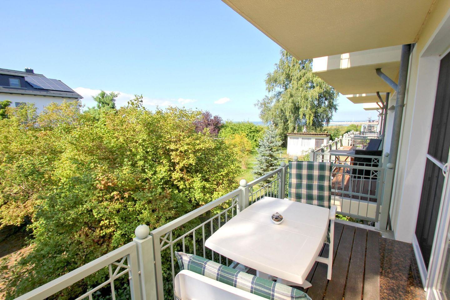 A balcony with a table and chairs, overlooking a garden and a building.