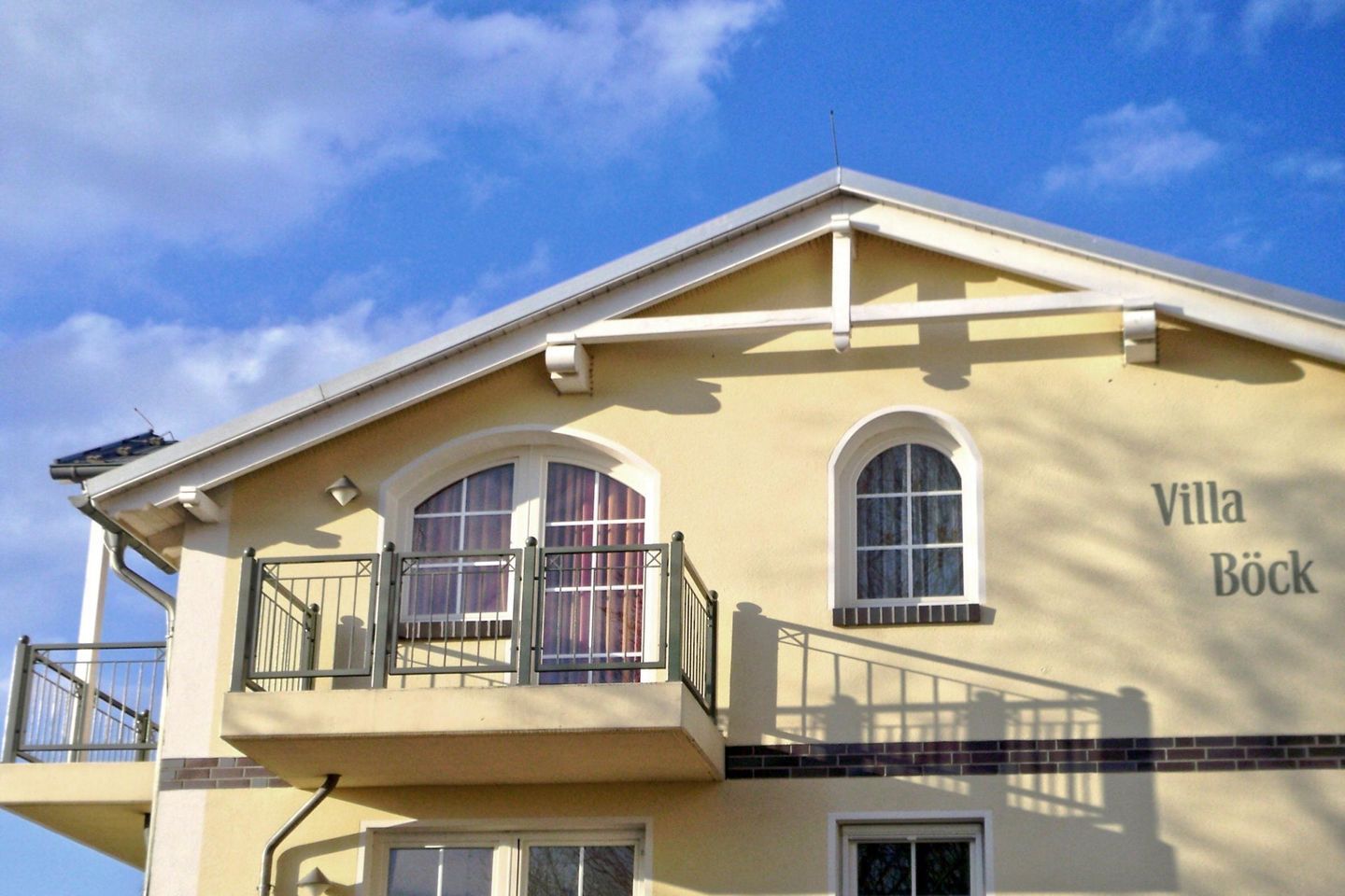 A two-story building with a balcony, a name plaque reading "Villa Bock," and a clear blue sky in the background.