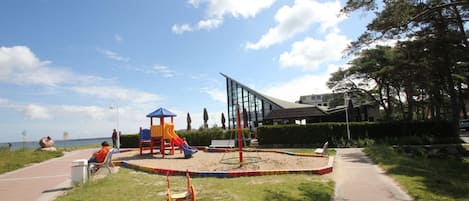 Ein Spielplatz mit Rutschen und Schaukeln, ein gepflasterter Weg und ein Gebäude im Hintergrund.