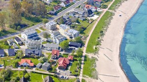 An aerial view of a coastal residential area with houses, a beach, and a road. - Directly behind the dune, with balcony and sea view - Strandvilla Böck FeWo 15 - (Glowe)