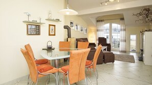 A dining area with a glass table and orange chairs, a sofa, and a chandelier. - Directly behind the dune, with balcony and sea view - Strandvilla Böck FeWo 15 - (Glowe)