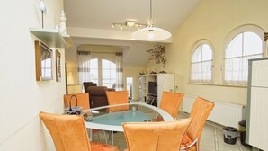 A dining area with a glass table surrounded by orange chairs, a white cabinet, and a radiator. - Directly behind the dune, with balcony and sea view - Strandvilla Böck FeWo 15 - (Glowe)