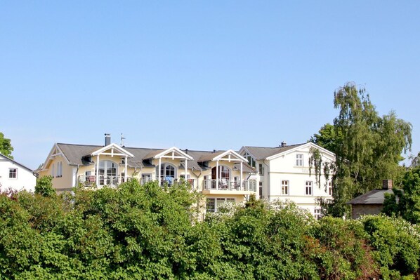 A row of multi-story houses with balconies, surrounded by dense greenery. - Directly behind the dune, with balcony and sea view - Strandvilla Böck FeWo 15 - (Glowe)